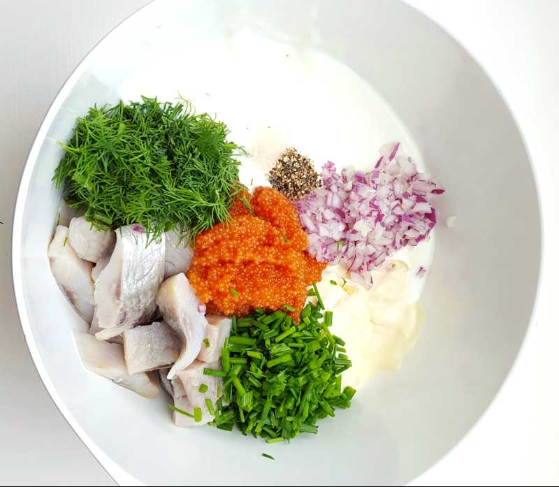 Skål med ingredienser för fiskröra, inklusive fisk, gräslök, rödlök och sås.